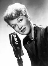 Black and white photo of Eve Arden leaning towards an old fashioned radio microphone.